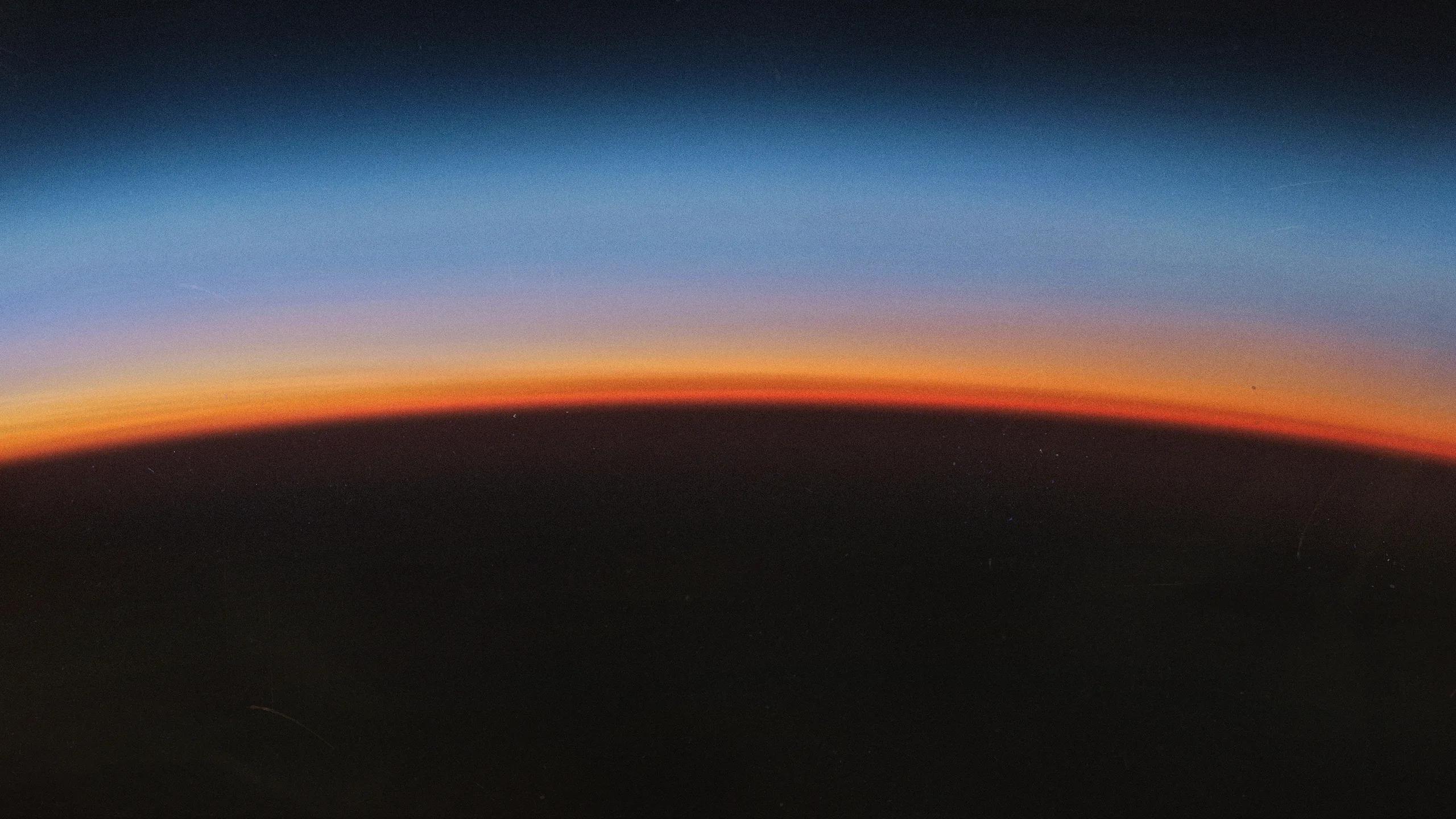 A curved horizon glowing orange beneath a deep blue sky above a dark foreground, from Anthropic’s Claude Opus 5.5 launch artwork.